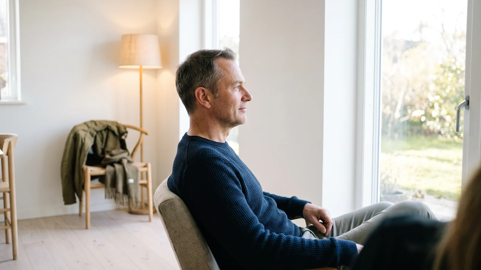 En lugn man i femtioårsåldern sitter avslappnad vid ett fönster och ser ut, utan oro