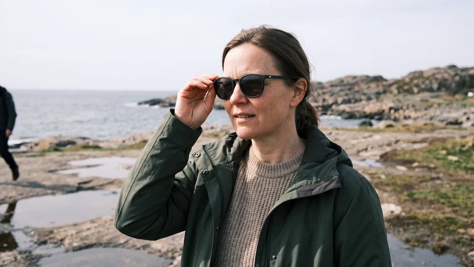 En kvinna i 40-årsåldern tar på sig solglasögon med UV-filter en solig dag vid kusten, skydd mot UV-strålar som kan ge pinguecula.
