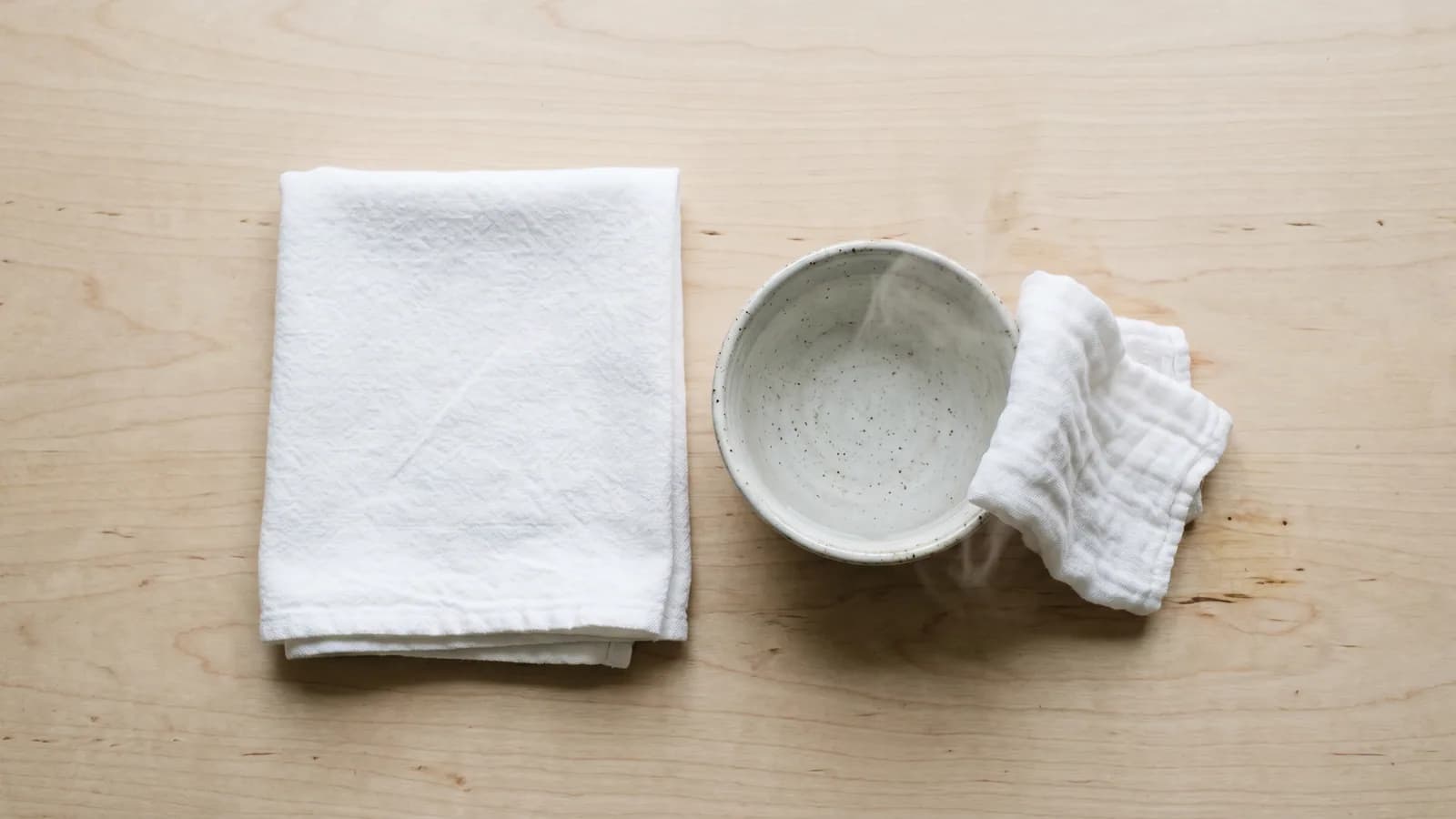 En ren hopvikt duk bredvid en skål med varmt vatten, sett ovanifrån